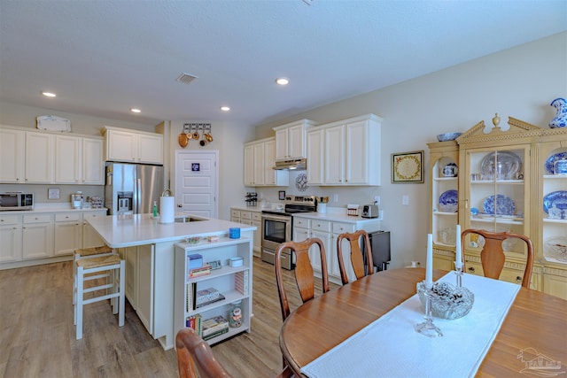 kitchen featuring appliances with stainless steel finishes, white cabinets, a kitchen breakfast bar, a kitchen island with sink, and light wood-type flooring