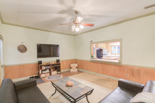 living room with ceiling fan, wood walls, and crown molding