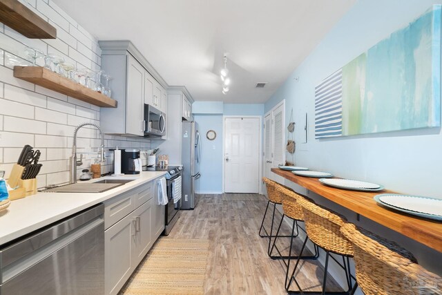 kitchen featuring gray cabinets, a breakfast bar area, light hardwood / wood-style flooring, stainless steel appliances, and backsplash