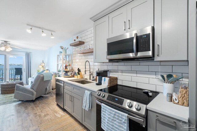 kitchen with light hardwood / wood-style floors, sink, decorative backsplash, appliances with stainless steel finishes, and ceiling fan