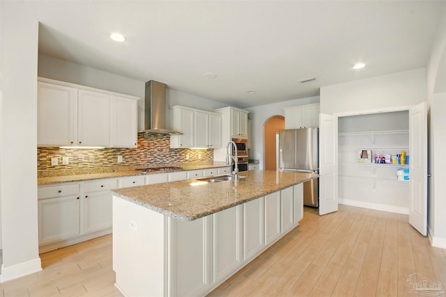 2665 Tulip Hill Rd, Pace, FL 32571 - kitchen with appliances with stainless steel finishes, wall chimney exhaust hood, a sink, arched walkways, and light wood-style floors