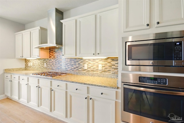 2665 Tulip Hill Rd, Pace, FL 32571 - kitchen featuring stainless steel appliances, wall chimney exhaust hood, tasteful backsplash, white cabinets, and light stone countertops