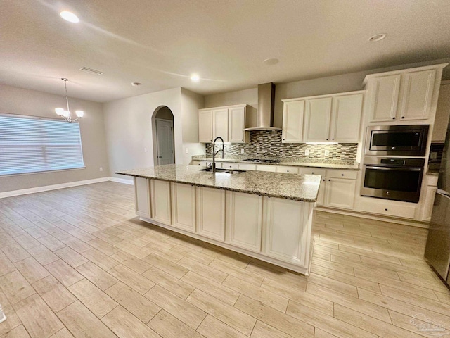 2665 Tulip Hill Rd, Pace, FL 32571 - kitchen featuring appliances with stainless steel finishes, a sink, wall chimney exhaust hood, arched walkways, and tasteful backsplash