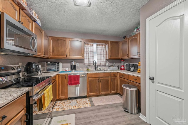 6856 Old W Ln, Milton, FL 32570 - kitchen featuring appliances with stainless steel finishes, a sink, a textured ceiling, light wood-type flooring, and brown cabinetry
