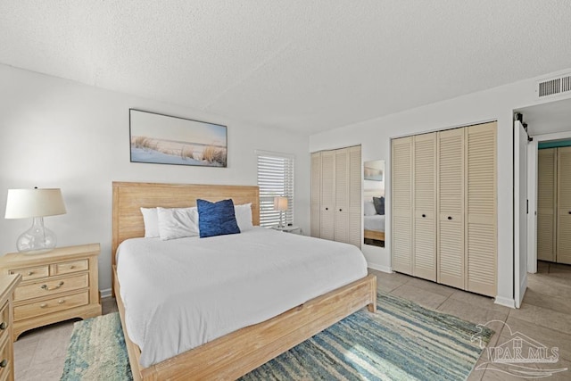 bedroom with multiple closets, light tile patterned floors, and a textured ceiling