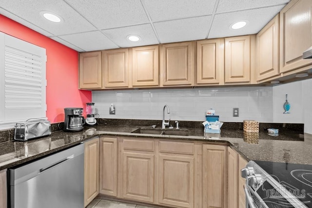 kitchen with sink, a paneled ceiling, appliances with stainless steel finishes, dark stone countertops, and backsplash