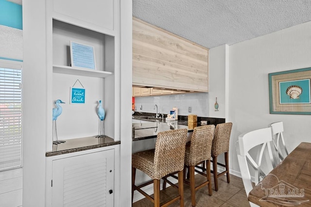 kitchen featuring light brown cabinetry, sink, tasteful backsplash, a textured ceiling, and light tile patterned floors