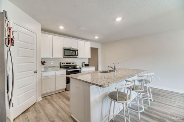 10885 Blacktail Loop, Pensacola, FL 32526 - kitchen featuring appliances with stainless steel finishes, a sink, light wood finished floors, a kitchen bar, and light stone countertops