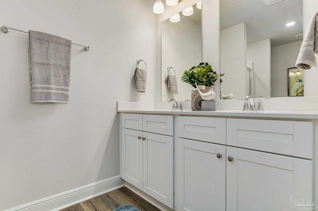 full bathroom with double vanity, baseboards, wood finished floors, and a sink