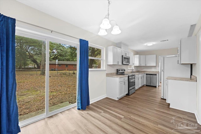 kitchen with stainless steel appliances, white cabinetry, sink, and pendant lighting