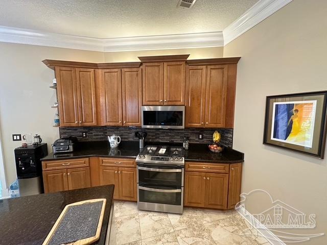 1988 Heritage Park Way, Navarre, FL 32566 - kitchen featuring stainless steel appliances, dark countertops, tasteful backsplash, brown cabinets, and crown molding