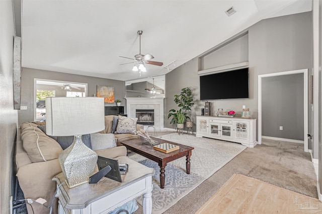 living room with a ceiling fan, carpet, a tiled fireplace, baseboards, and lofted ceiling