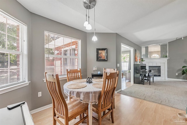 dining room featuring a tile fireplace, baseboards, light wood-style floors, and a healthy amount of sunlight