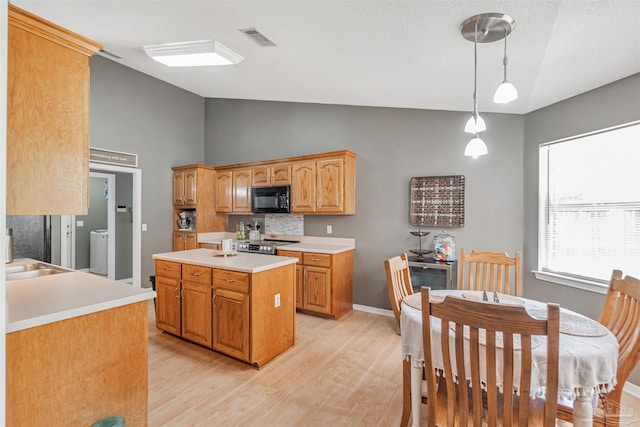 kitchen featuring black microwave, light wood-style floors, light countertops, lofted ceiling, and visible vents