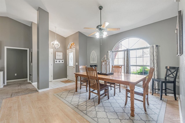 dining room with ceiling fan with notable chandelier, light wood-style flooring, baseboards, and high vaulted ceiling