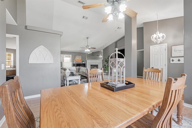 dining room featuring visible vents, a ceiling fan, baseboards, a fireplace, and high vaulted ceiling