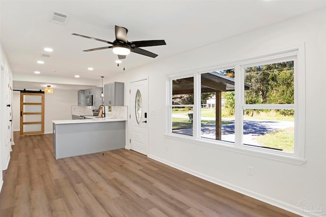 kitchen featuring kitchen peninsula, gray cabinetry, wood-type flooring, and a barn door