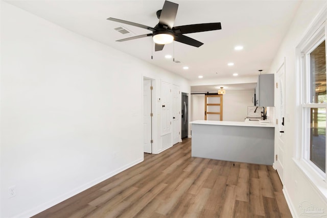 interior space featuring hardwood / wood-style flooring, ceiling fan, stainless steel fridge, a barn door, and kitchen peninsula