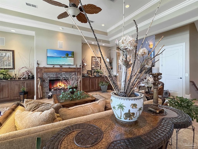 living room featuring a fireplace, visible vents, a raised ceiling, and ornamental molding