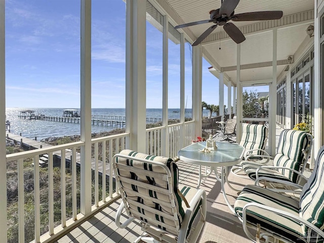 sunroom with a water view, a view of the beach, and a ceiling fan