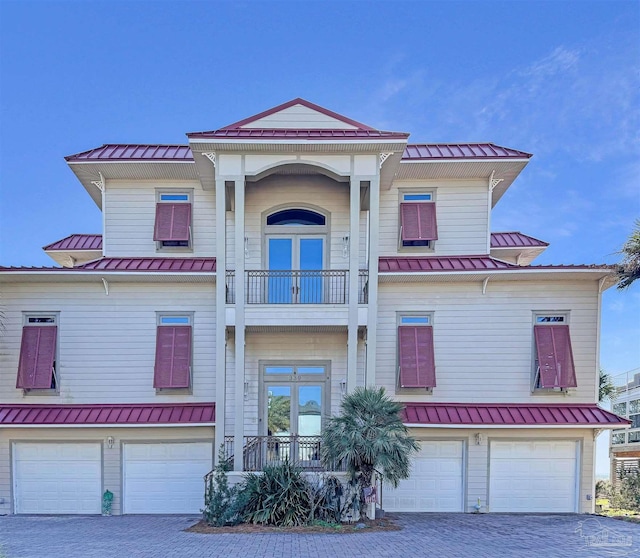 view of front facade with metal roof, an attached garage, a balcony, french doors, and a standing seam roof