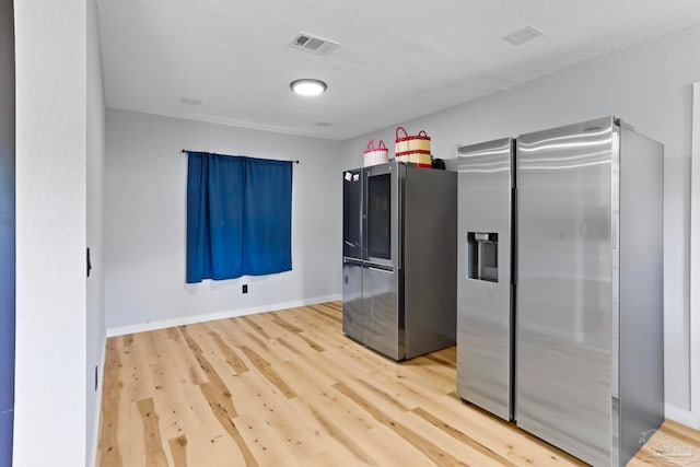 kitchen featuring stainless steel fridge, a textured ceiling, and light wood-type flooring