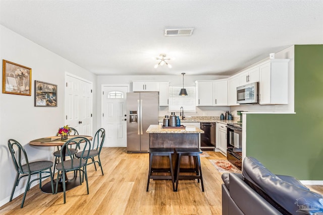 kitchen with a center island, light wood finished floors, visible vents, white cabinetry, and black appliances