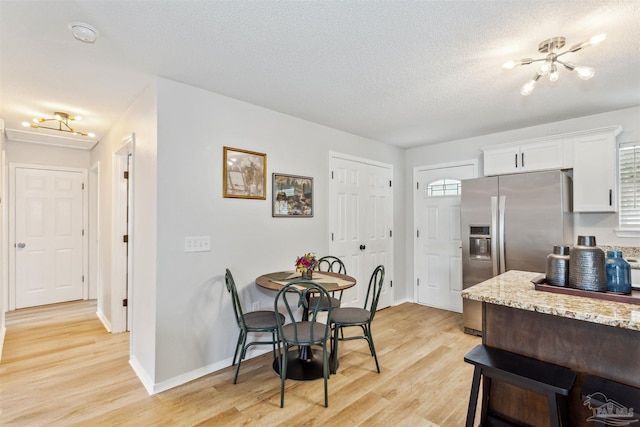 dining space with light wood-style floors, a chandelier, a textured ceiling, and baseboards