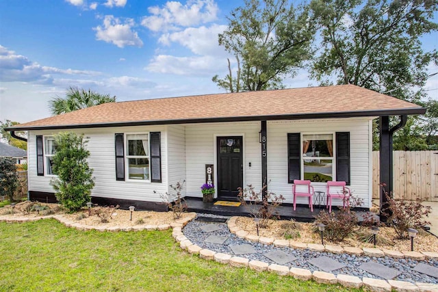 ranch-style home with covered porch, roof with shingles, fence, and a front yard