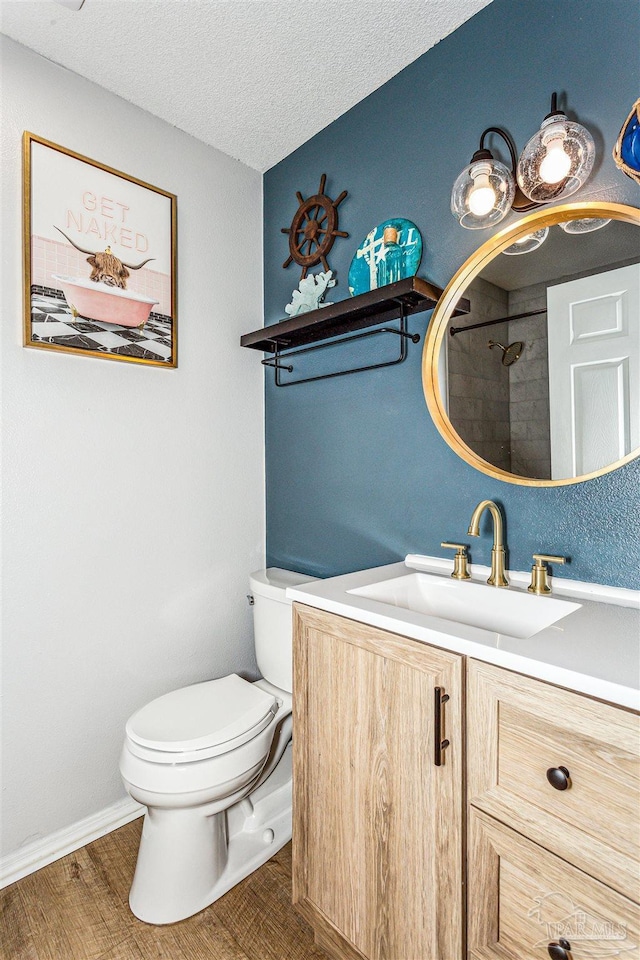 bathroom featuring a textured ceiling, toilet, wood finished floors, vanity, and walk in shower