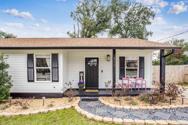 view of front of home featuring covered porch, a shingled roof, and fence