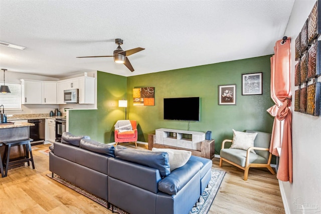 living area featuring a ceiling fan, baseboards, a textured ceiling, and light wood finished floors