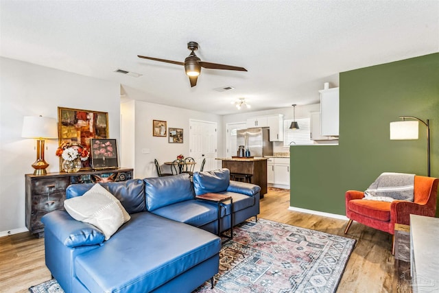 living room with a textured ceiling, light wood finished floors, visible vents, and a ceiling fan