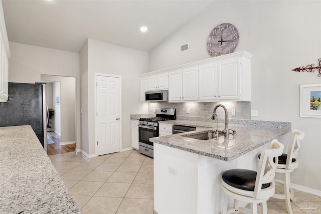 kitchen featuring light tile patterned floors, kitchen peninsula, appliances with stainless steel finishes, white cabinets, and sink