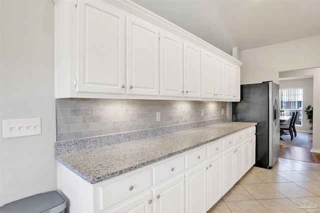 kitchen with stainless steel fridge with ice dispenser, backsplash, white cabinets, and light stone countertops