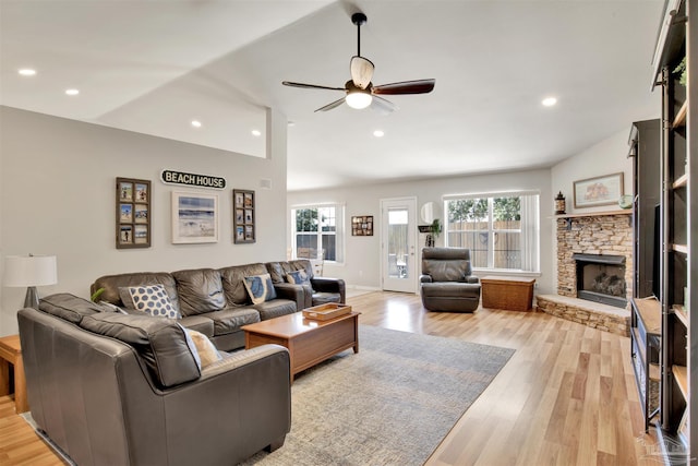 living room featuring vaulted ceiling, ceiling fan, light hardwood / wood-style floors, and a stone fireplace