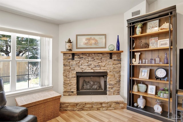 living area featuring plenty of natural light, lofted ceiling, hardwood / wood-style flooring, and a stone fireplace