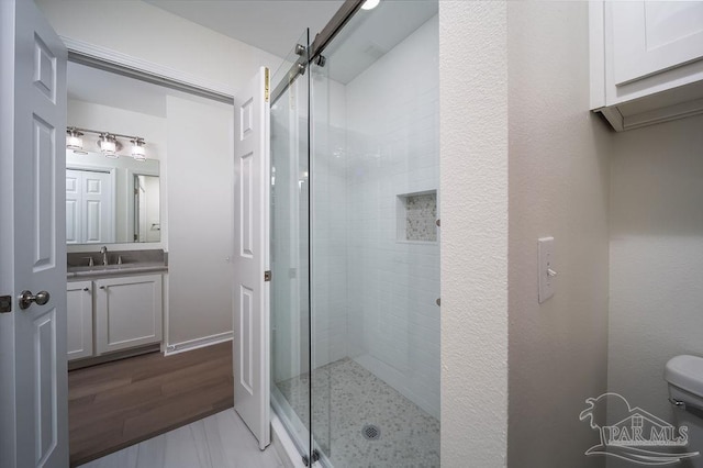 bathroom featuring vanity, toilet, wood finished floors, and a stall shower