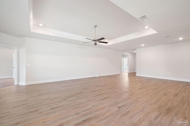 unfurnished living room with crown molding, ceiling fan, a raised ceiling, and light hardwood / wood-style flooring