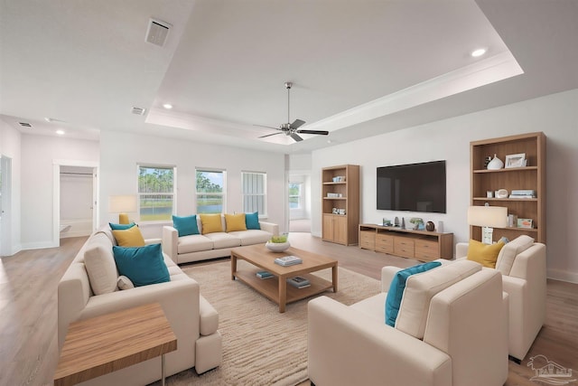 living room with ceiling fan, a raised ceiling, and light wood-type flooring