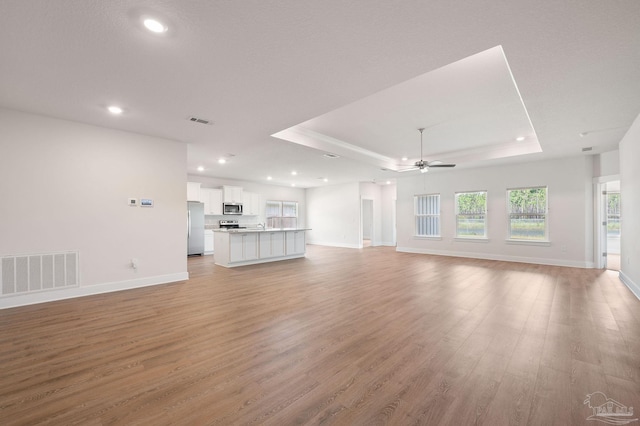 unfurnished living room featuring ceiling fan, a raised ceiling, and light wood-type flooring