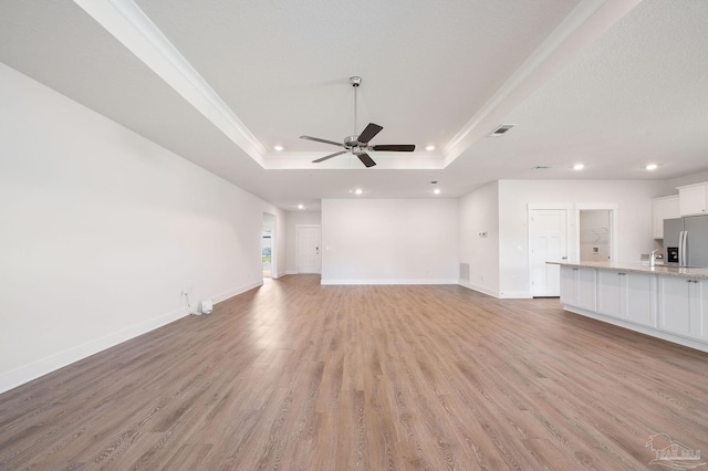 unfurnished living room featuring ornamental molding, light hardwood / wood-style floors, a raised ceiling, and ceiling fan