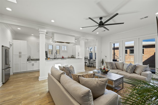 living room with crown molding, plenty of natural light, decorative columns, and light hardwood / wood-style flooring