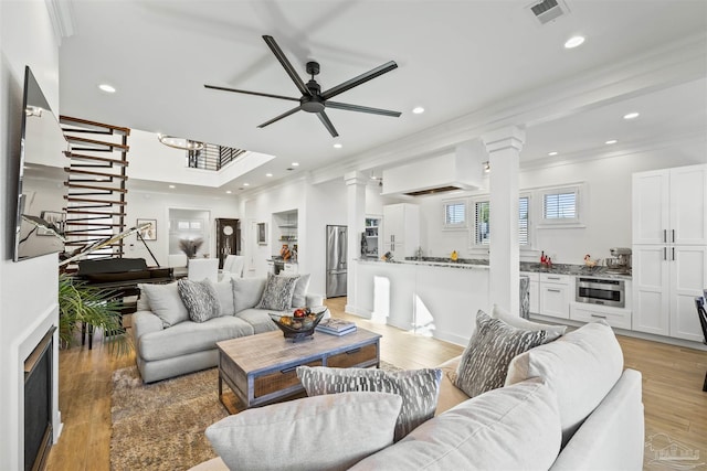 living room with decorative columns, ornamental molding, ceiling fan, and light hardwood / wood-style flooring