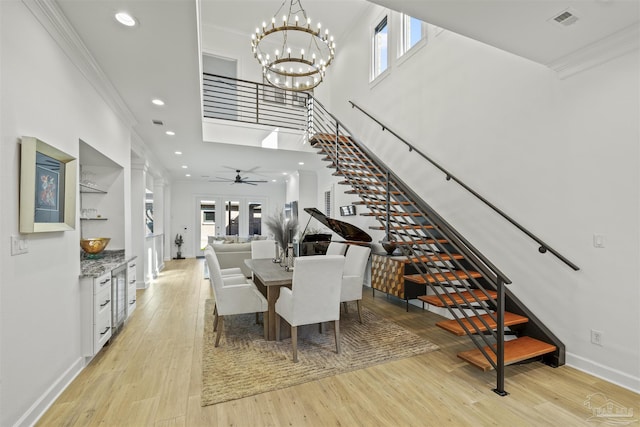 dining space featuring crown molding, light hardwood / wood-style flooring, ceiling fan with notable chandelier, and a high ceiling