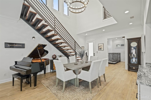 dining space featuring a towering ceiling, ornamental molding, light hardwood / wood-style flooring, and a notable chandelier