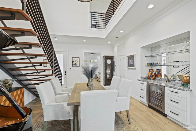 dining area with crown molding, indoor bar, beverage cooler, and light hardwood / wood-style flooring