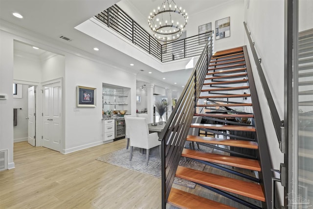 stairs featuring wood-type flooring, ornamental molding, a notable chandelier, a towering ceiling, and beverage cooler