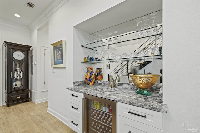 bar with light hardwood / wood-style flooring, stone counters, ornamental molding, white cabinets, and beverage cooler