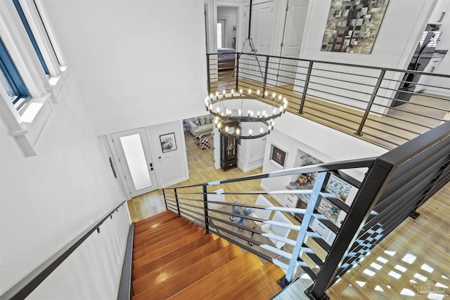 stairs featuring an inviting chandelier, a towering ceiling, and wood-type flooring